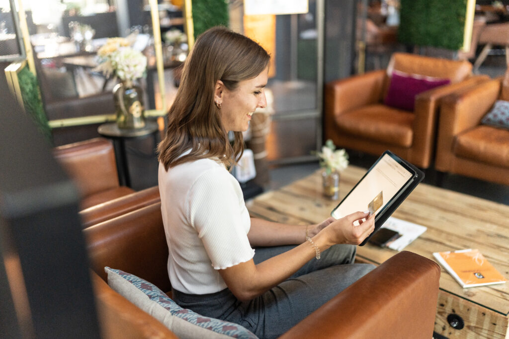 Eine Frau hält ein Tablet und eine Kreditkarte in der Hand und lächelt.